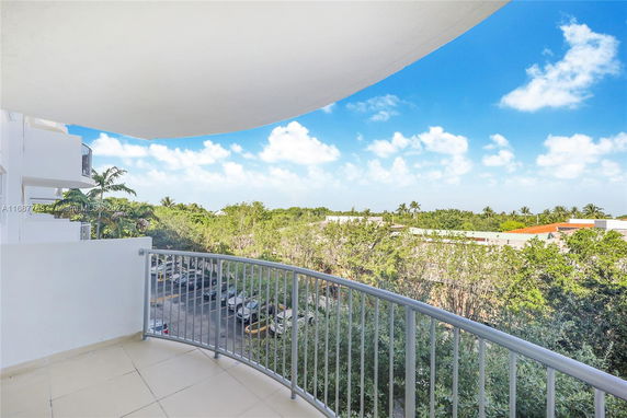 View from a balcony showing a parking area and green landscape with trees.