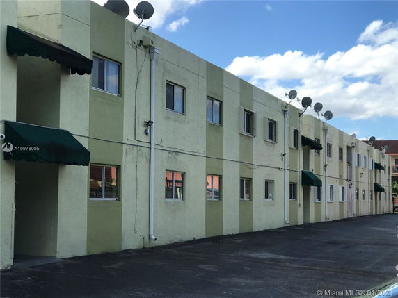 Front view of a multi-story apartment building with green awnings and satellite dishes on the roof.