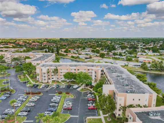 Aerial view of a large apartment complex with visible rooftops, parking area, and surrounding neighborhood.