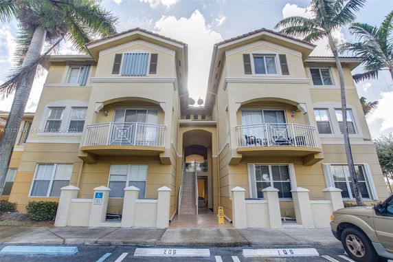 Front view of a multi-story residential building with balconies and stairway entrance.