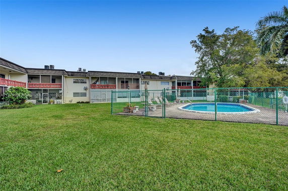 Outdoor area with a swimming pool surrounded by a fence, adjacent to a two-story building.