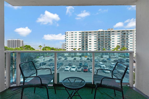 View of surrounding area from a balcony, showing a parking lot and a high-rise residential building.