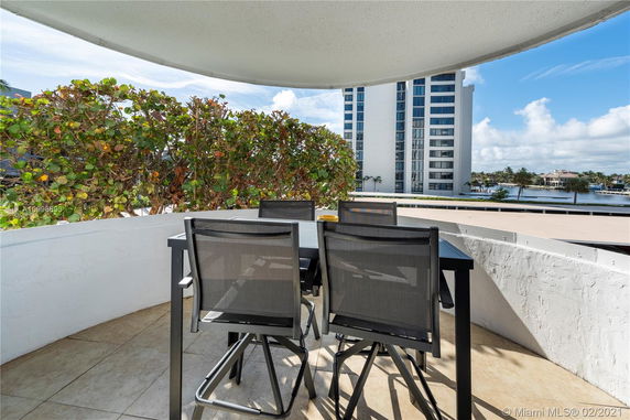 Outdoor terrace with chairs and a table, overlooking a waterway and modern buildings.