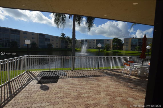 View of a patio overlooking a pond with nearby buildings and a fountain.