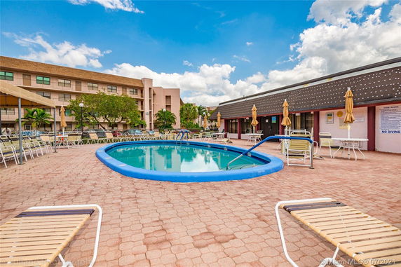 Outdoor pool area with surrounding seating next to a multi-story building.