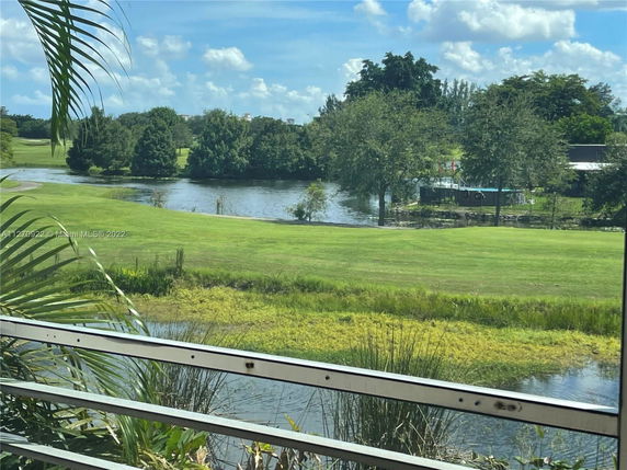 Panoramic outdoor view of a grassy area with a lake and trees in the background.