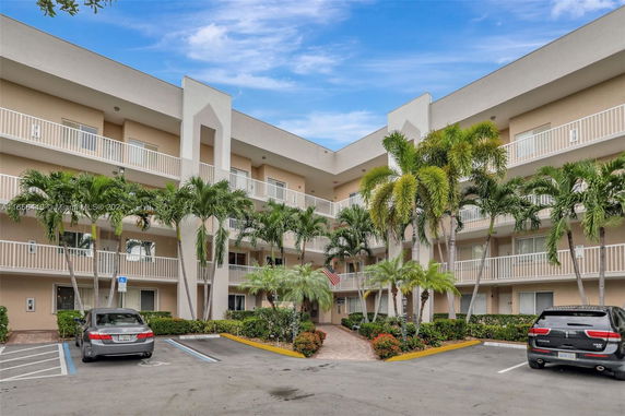 Front view of a multi-story building with balconies and palm trees in front.