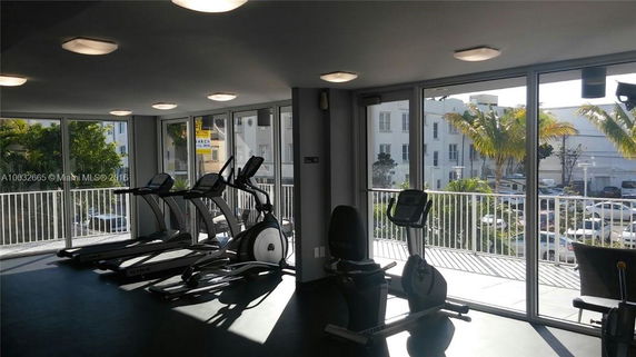 Indoor gym with exercise equipment and large windows overlooking the outside.