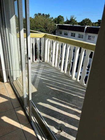View from a balcony with white railing looking out at nearby buildings and trees.