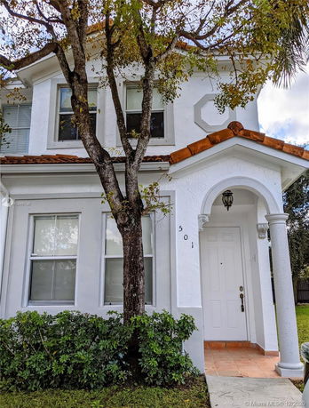 Front view of a two-story house with a white exterior and Spanish-style roof tiles.