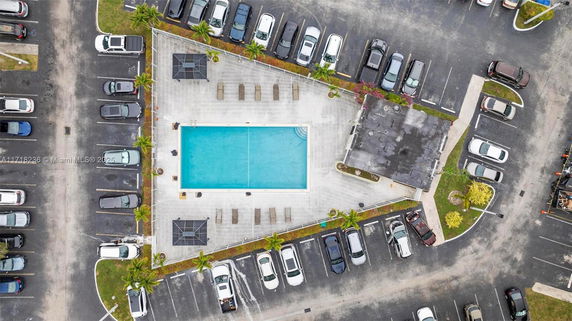 Aerial view of a swimming pool with surrounding lounge chairs and nearby parking area.