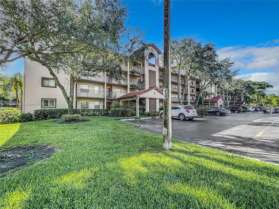 Front view of a multi-story residential building with balconies and adjacent parking area.