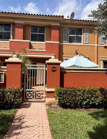 Front view of a two-story house with a small fenced entrance and red-orange exterior.