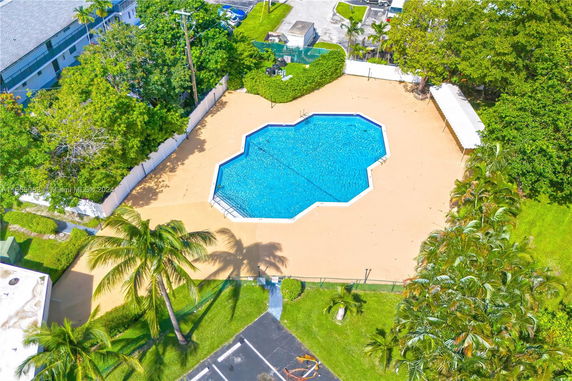 Aerial view of an outdoor swimming pool with surrounding patio area and lush greenery.