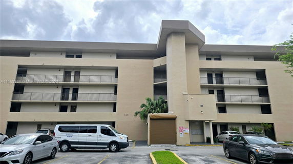 Front view of a multi-story apartment building with balconies and a parking area.