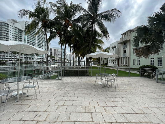 Outdoor area with umbrellas and tables overlooking a waterfront with buildings in the background.