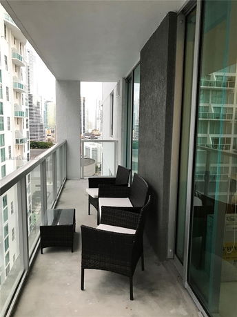 Balcony view from a high-rise apartment with outdoor seating and glass railing.
