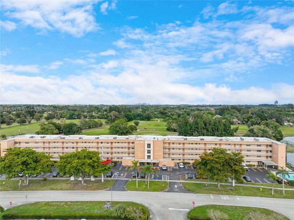 Front view of a multi-story building with a parking area and trees in front.
