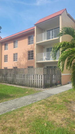 Front view of a multi-story building with balconies and a fenced area.