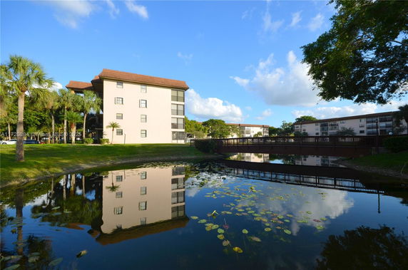 Front view of a multi-story building near a pond with a footbridge.
