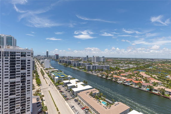 Aerial view of a cityscape with high-rise buildings, a canal, and surrounding urban areas.