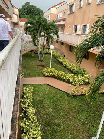 View of a multi-story building with balconies surrounded by pathways and landscaped gardens.