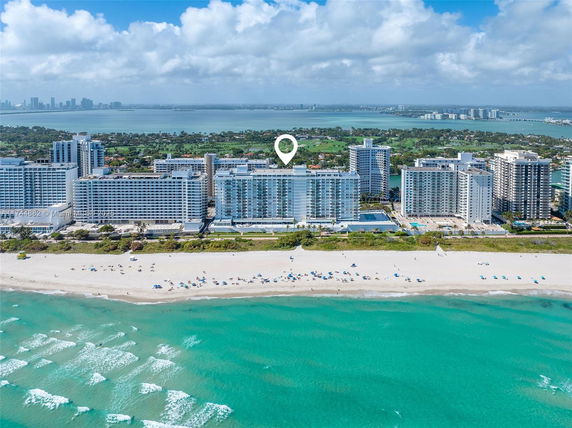 Aerial view of beachfront buildings with the ocean and distant cityscape in the background.