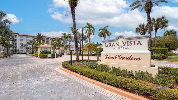Front view of a multi-story residential building with palm trees and a welcome sign for Gran Vista at Doral Gardens.