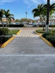 View of a walkway with palm trees leading to a parking area and buildings in the background.