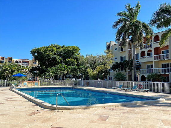 Outdoor swimming pool area with nearby residential buildings and palm trees.