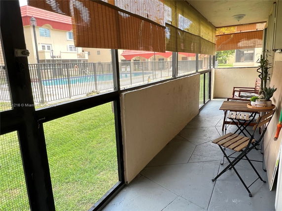 Enclosed patio area with a view of an outdoor swimming pool and apartment buildings.