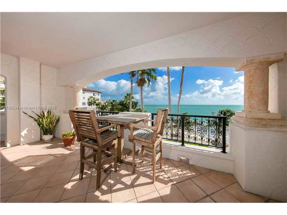 Outdoor patio with wooden furniture, offering a panoramic view of the ocean and palm trees.