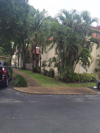 Front view of a two-story residential building with a red roof and surrounded by tall palm trees.