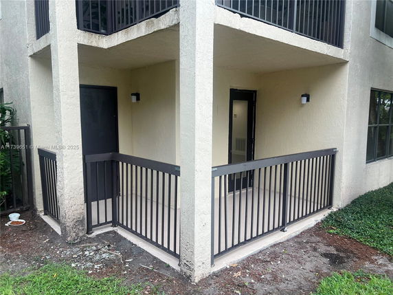 Exterior view of a building with balconies and a small fenced area.