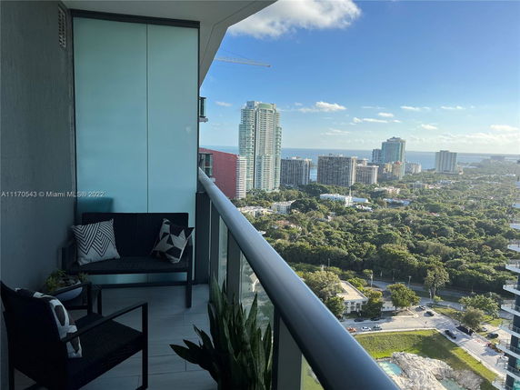 Outdoor balcony view overlooking urban and green areas with buildings in the distance.
