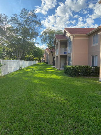 Side view of multi-story buildings with balconies, set against a clear sky, surrounded by green grass and trees.