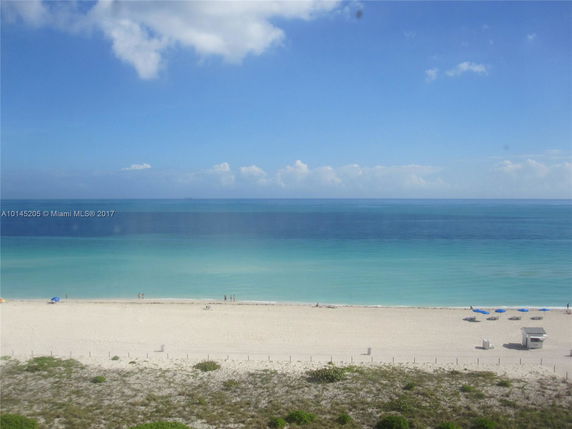 View of a sandy beach and the ocean under a clear blue sky.