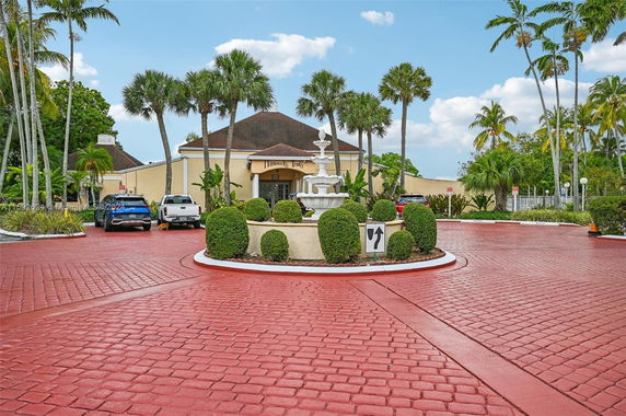 Front view of a building with a fountain and driveway surrounded by palm trees.