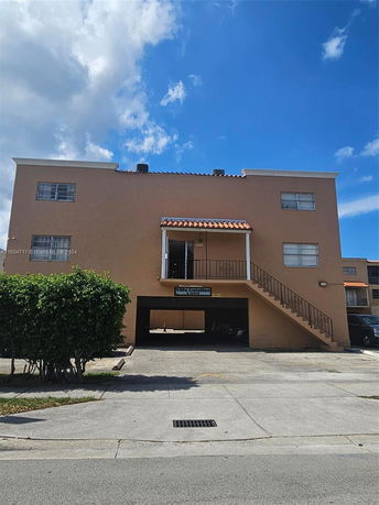 Front view of a two-story building with external stairs and a garage entrance.