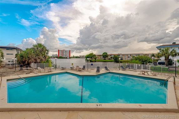 Outdoor swimming pool area with surrounding lounge chairs and a view of the water and buildings.