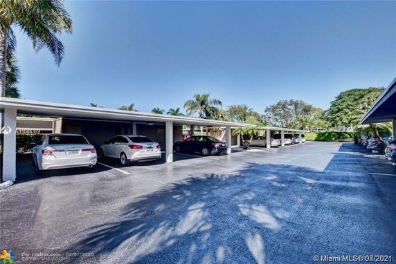 View of a carport with multiple parked cars under a flat roof structure.