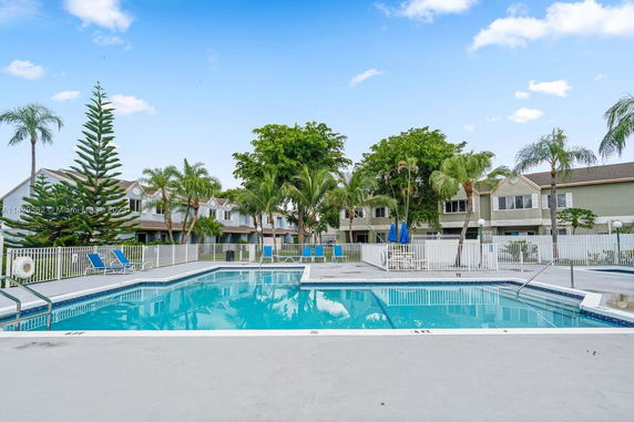 Outdoor swimming pool surrounded by fencing, with residential buildings in the background.