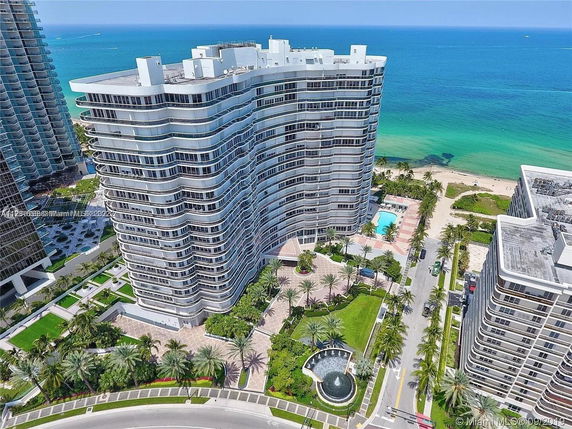 Aerial view of a modern high-rise residential building with curved balconies near the beach.