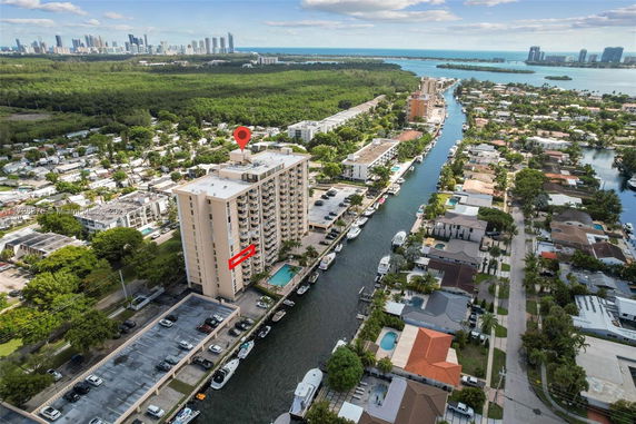 Aerial view of a multi-story apartment building next to a canal, surrounded by residential houses.