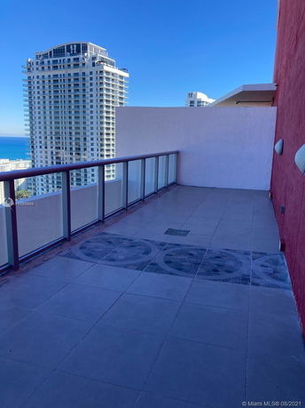 Rooftop view with glass railing and tiled flooring, overlooking a high-rise building in the background.