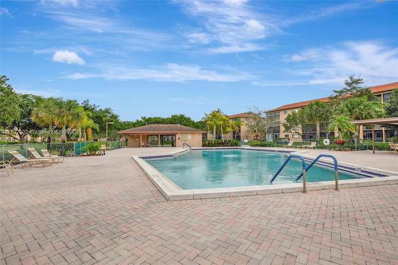 Outdoor swimming pool area with surrounding buildings and palm trees.