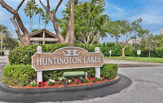 Entrance sign for Huntington Lakes with trees and a glimpse of nearby buildings.
