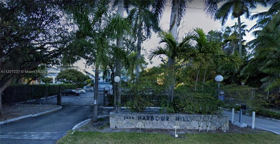 Front view of a gated residential building with a sign reading 'Harbour Hill' and palm trees.