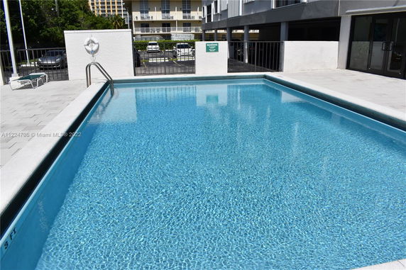 Outdoor swimming pool with railing and surrounding buildings.