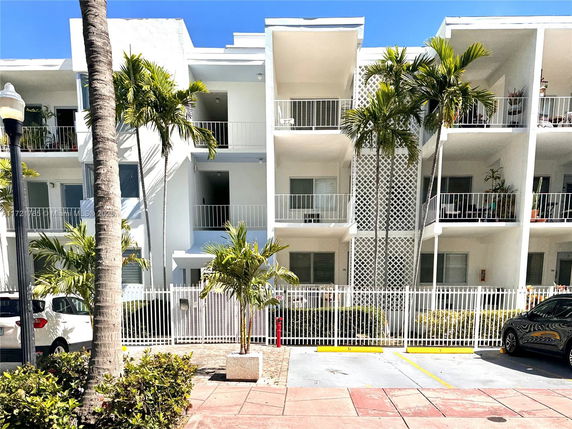 Front view of a three-story apartment building with balconies and white fencing.